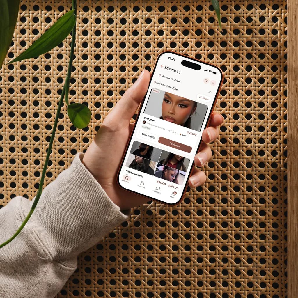 Client's hand holding a phone showing a clean beauty booking calendar and time slots